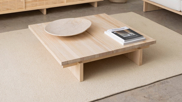 Close-up of a cream wool rug with a light wood coffee table and decorative bowl in a minimalist living room